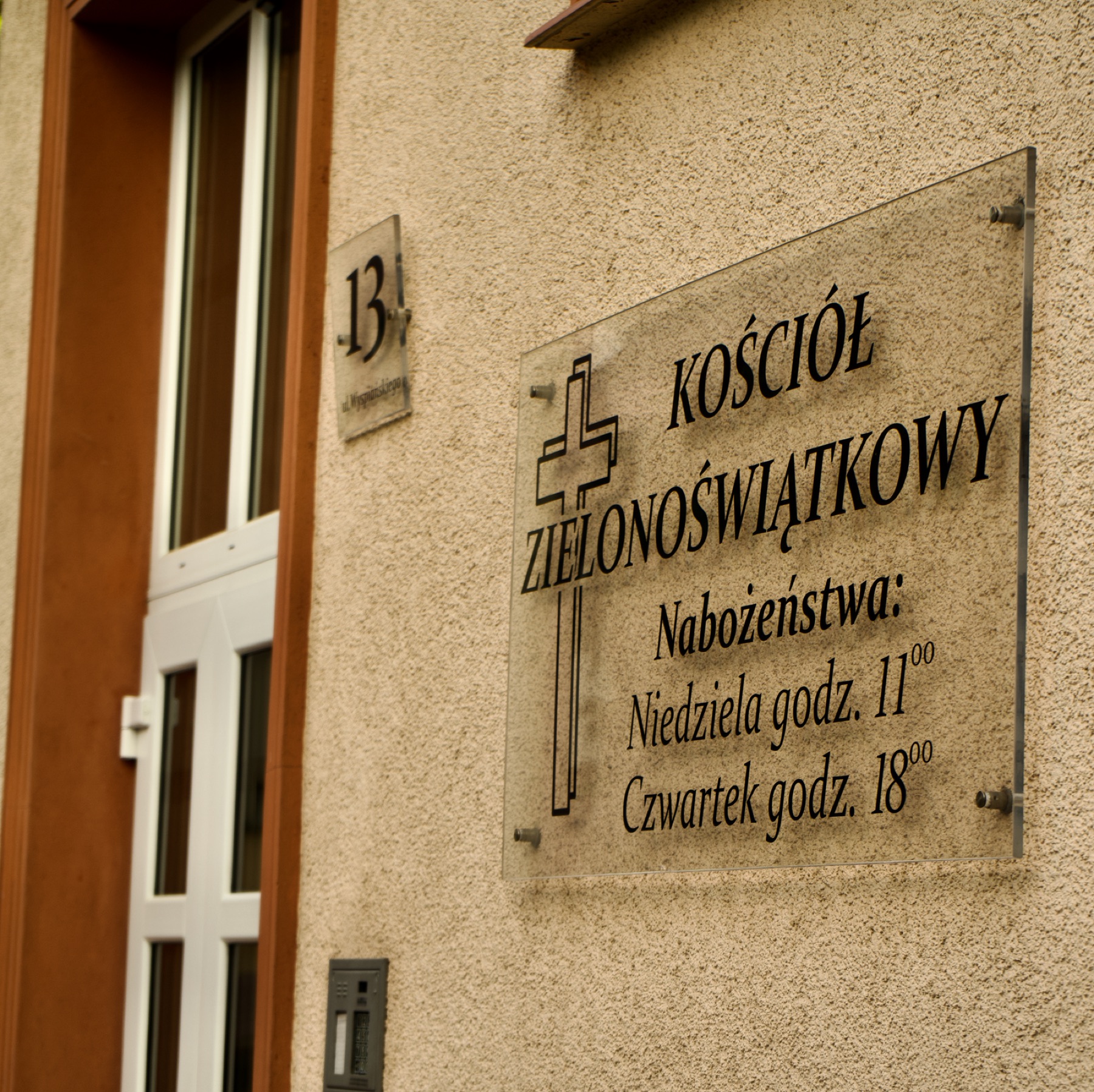 Szklana tabliczka z napisem Kościół Zielonoświątkowy oraz godzinami nabożeństw: niedziela 11:00, czwartek 18:00.